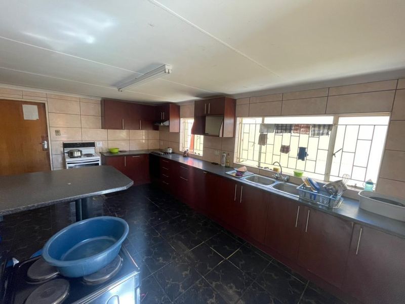 A functional kitchen featuring dark wood cabinetry, tiled splashbacks, a double basin sink, and tiled flooring, offering potential for a modern renovation.