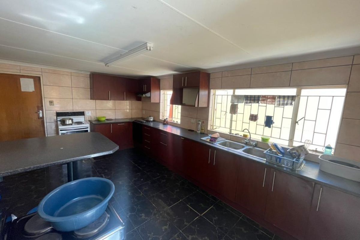 A functional kitchen featuring dark wood cabinetry, tiled splashbacks, a double basin sink, and tiled flooring, offering potential for a modern renovation.