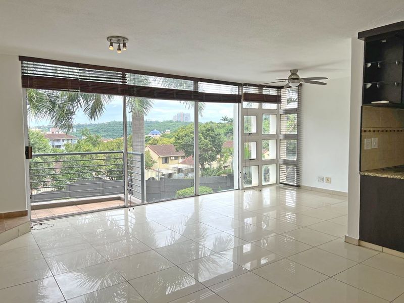 Spacious open-plan living area featuring polished tile floors, a ceiling fan, and large glass sliding doors opening to a balcony with scenic views.
