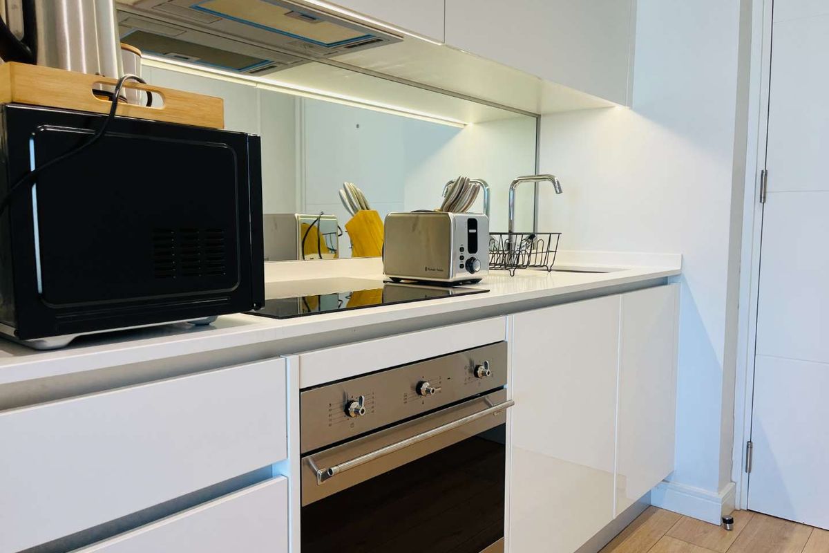 Modern kitchen featuring sleek handleless white cabinetry, integrated appliances, induction hob, and a contemporary mirror splashback.