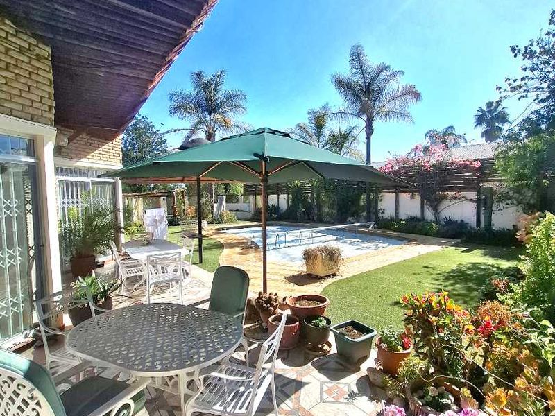 A covered patio area overlooking a private swimming pool and landscaped garden, featuring patterned tile flooring and direct access to the main house.