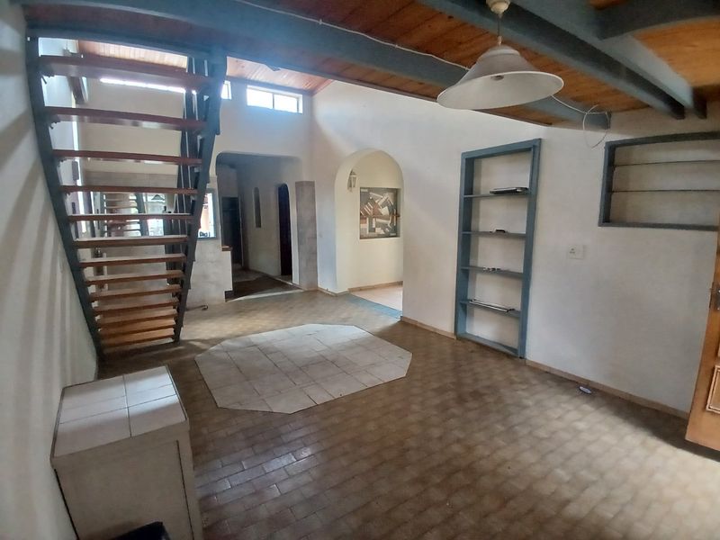 Spacious living area featuring an open tread staircase, exposed timber ceiling beams, and unique arched architectural details throughout the open-plan layout.