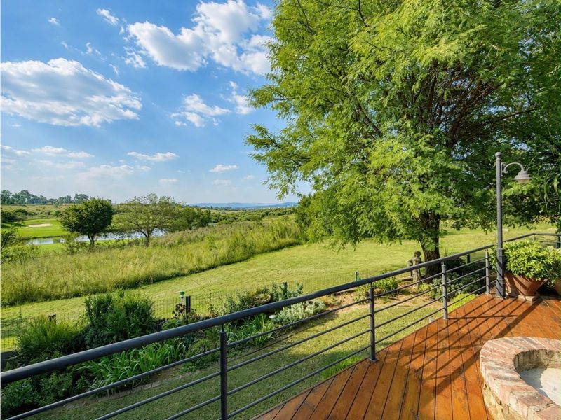 A spacious wooden deck featuring a built-in brick fire pit, overlooking a lush green landscape and golf course.