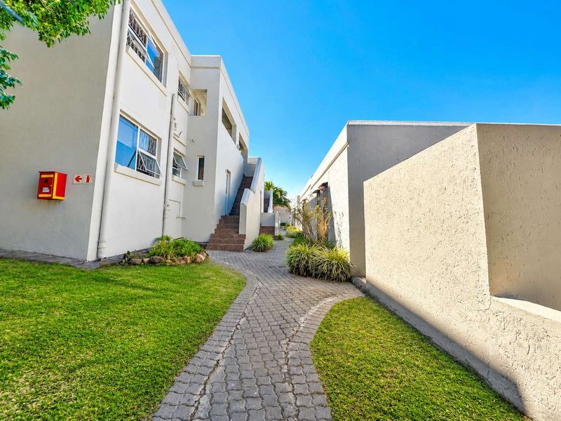 Exterior view of the apartment complex featuring a paved walkway, landscaped lawn, and external staircase access to upper units.