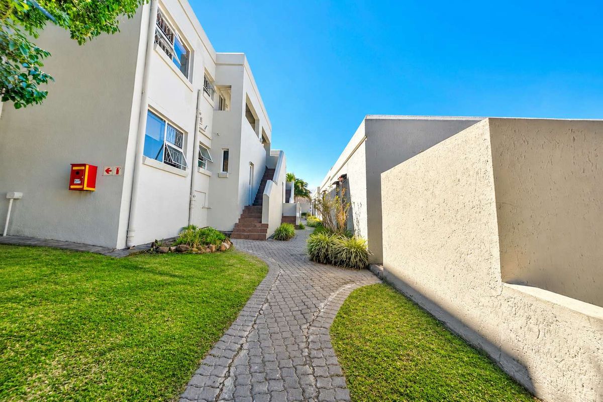 Exterior view of the apartment complex featuring a paved walkway, landscaped lawn, and external staircase access to upper units.