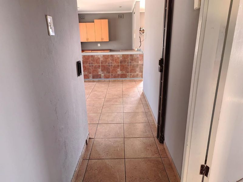 An open-plan living and kitchen area featuring tiled flooring, a tiled breakfast bar, and wooden cabinetry, presented in a vacant, ready-to-renovate condition.