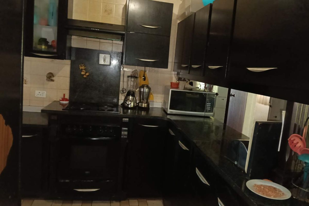 A functional kitchen featuring dark built-in cabinetry, granite countertops, a built-in oven, and a hob with an extractor fan.