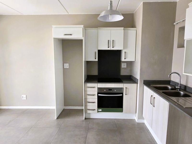 Modern kitchen featuring built-in cabinetry, integrated oven and hob, stainless steel double sink, and neutral tiled flooring in an open-plan layout.