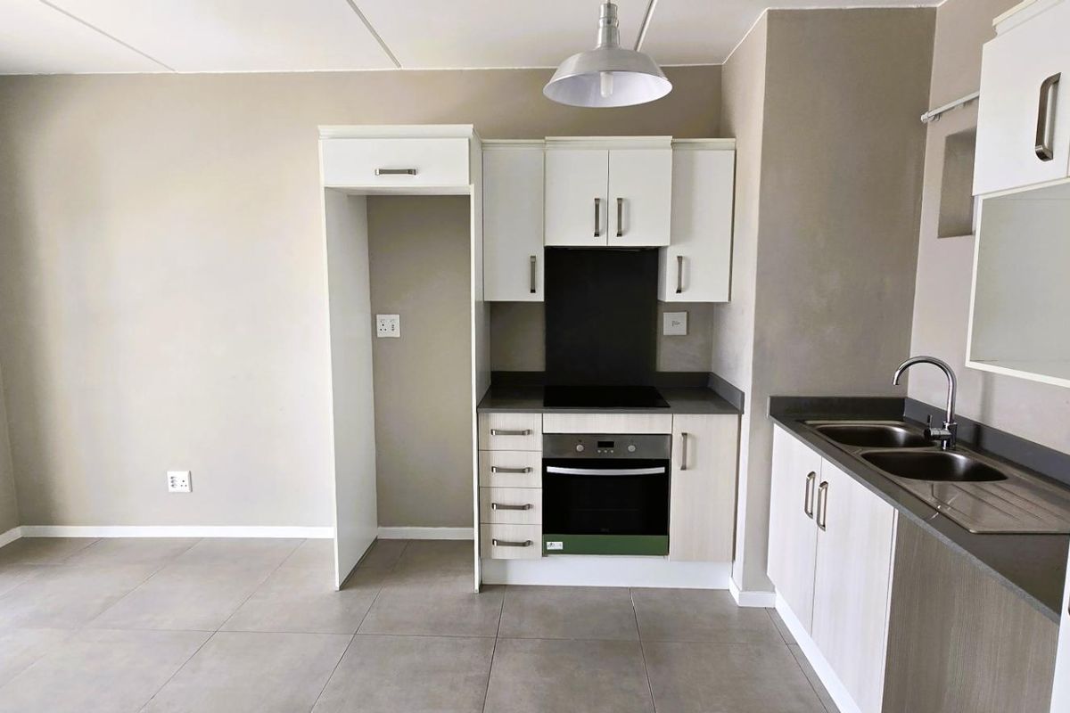 Modern kitchen featuring built-in cabinetry, integrated oven and hob, stainless steel double sink, and neutral tiled flooring in an open-plan layout.