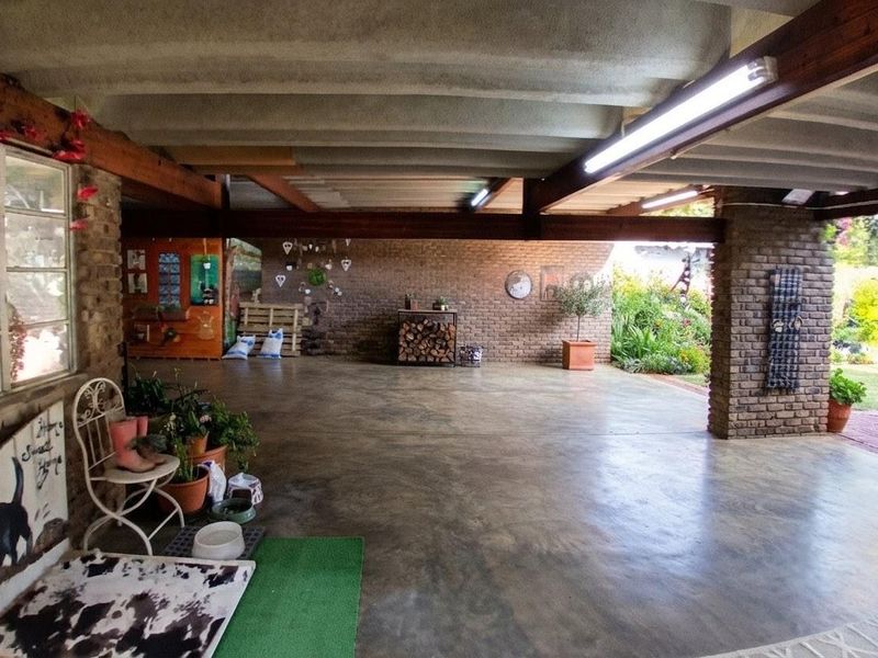 A spacious covered patio featuring exposed timber beams, brick walls, and polished concrete flooring, offering a versatile outdoor entertainment area overlooking the garden.