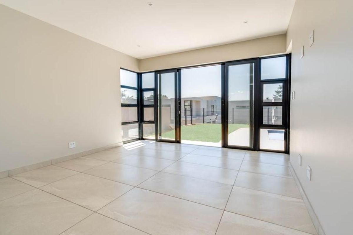 A bright, modern, and empty living room featuring large black-framed sliding glass doors that open directly onto a private garden area.