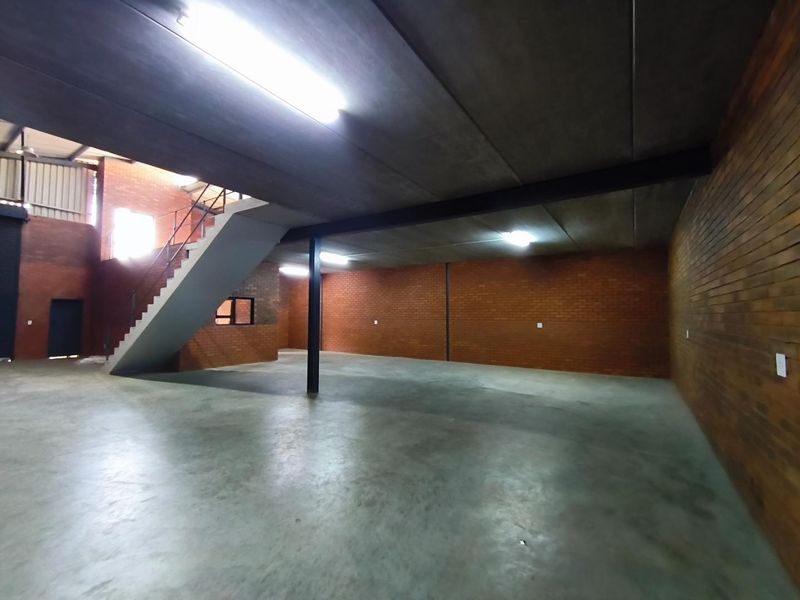 Spacious industrial open-plan area featuring polished concrete floors, exposed brick walls, and a mezzanine level accessed by a steel staircase.