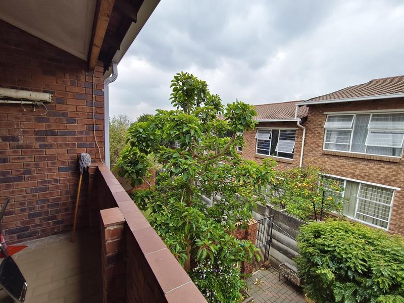 A functional balcony with brick balustrade and tiled flooring, overlooking the complex garden area.