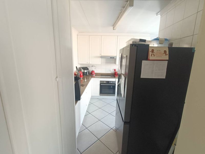 A functional galley-style kitchen featuring white cabinetry, built-in oven and hob, tiled backsplash, and tiled flooring.