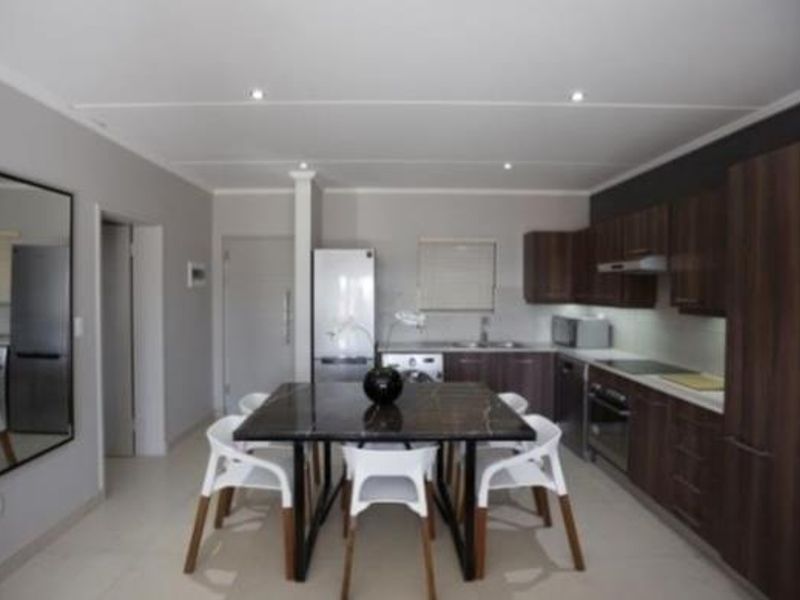 Modern open-plan kitchen and dining area featuring dark wood cabinetry, integrated appliances, tiled flooring, and recessed lighting.