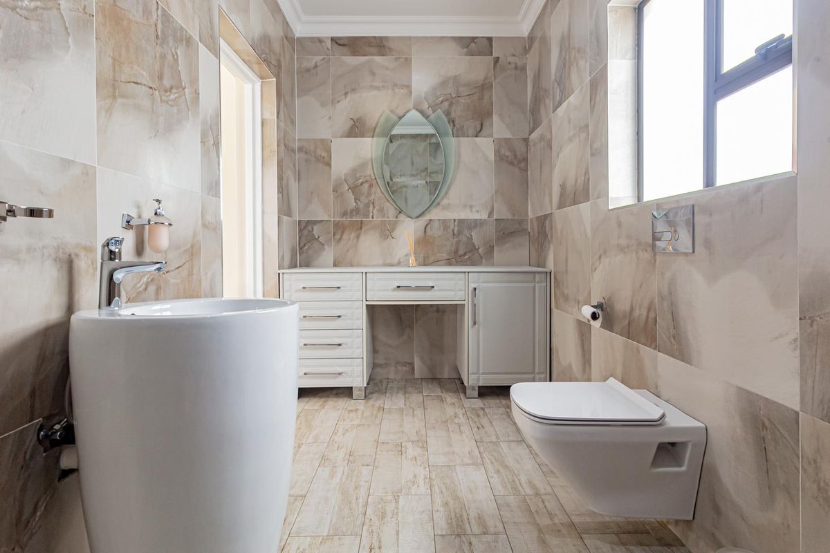 Modern bathroom featuring floor-to-ceiling marble-look tiling, a wall-mounted toilet, a sleek vanity unit, and a contemporary freestanding basin.