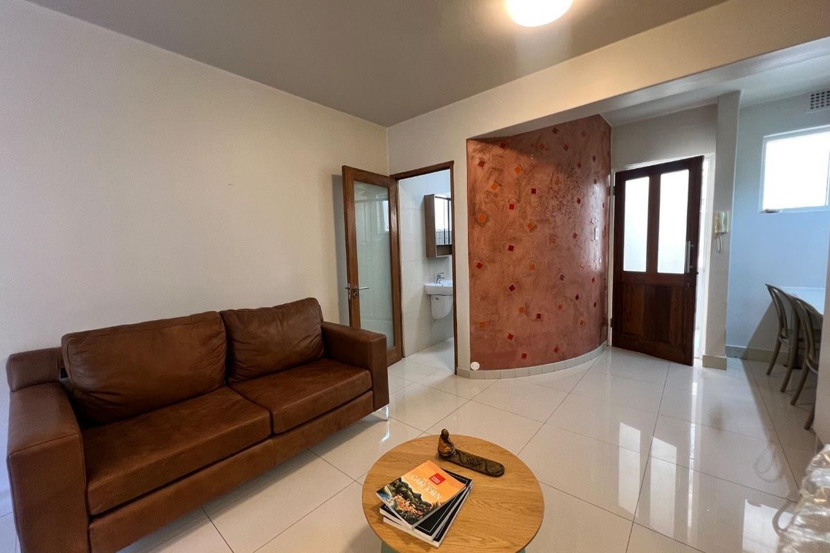 Living area featuring polished tile flooring, a distinctive textured feature wall, and access to an adjacent bathroom and entrance.
