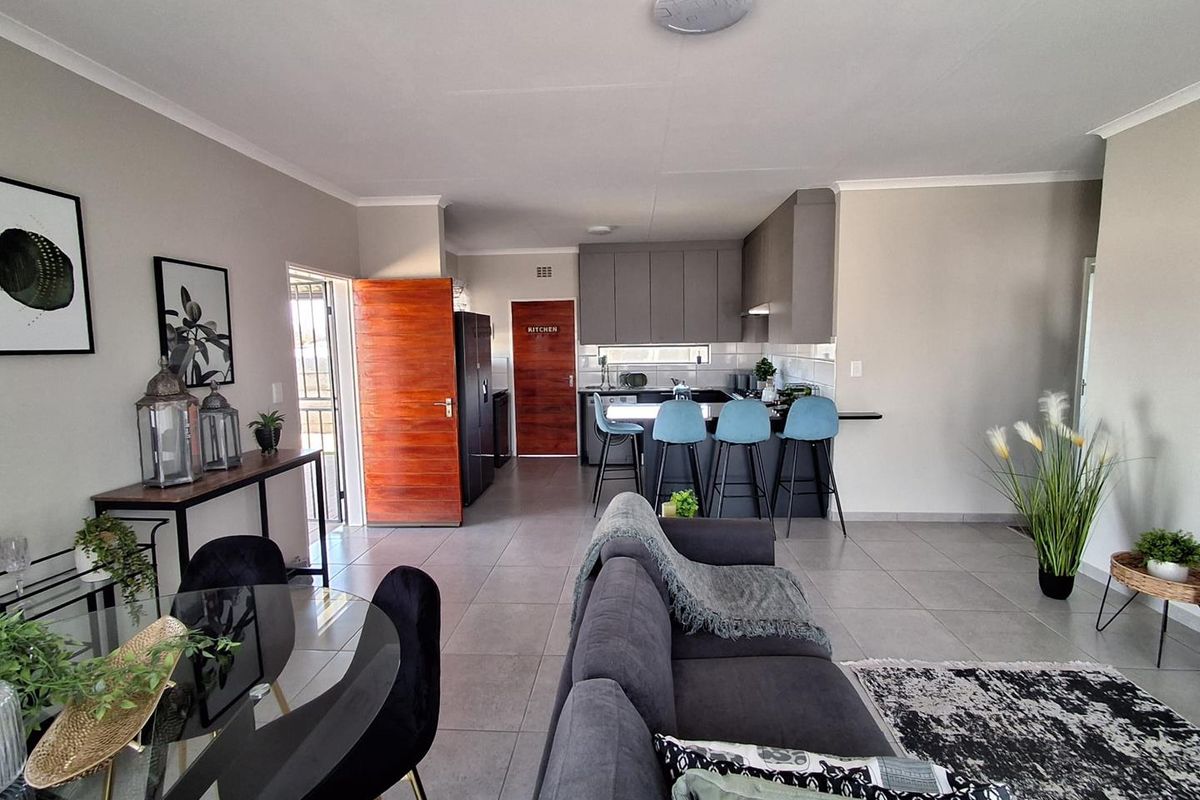 An open-plan living and kitchen area featuring modern grey cabinetry, a breakfast bar, and neutral tiled flooring throughout.