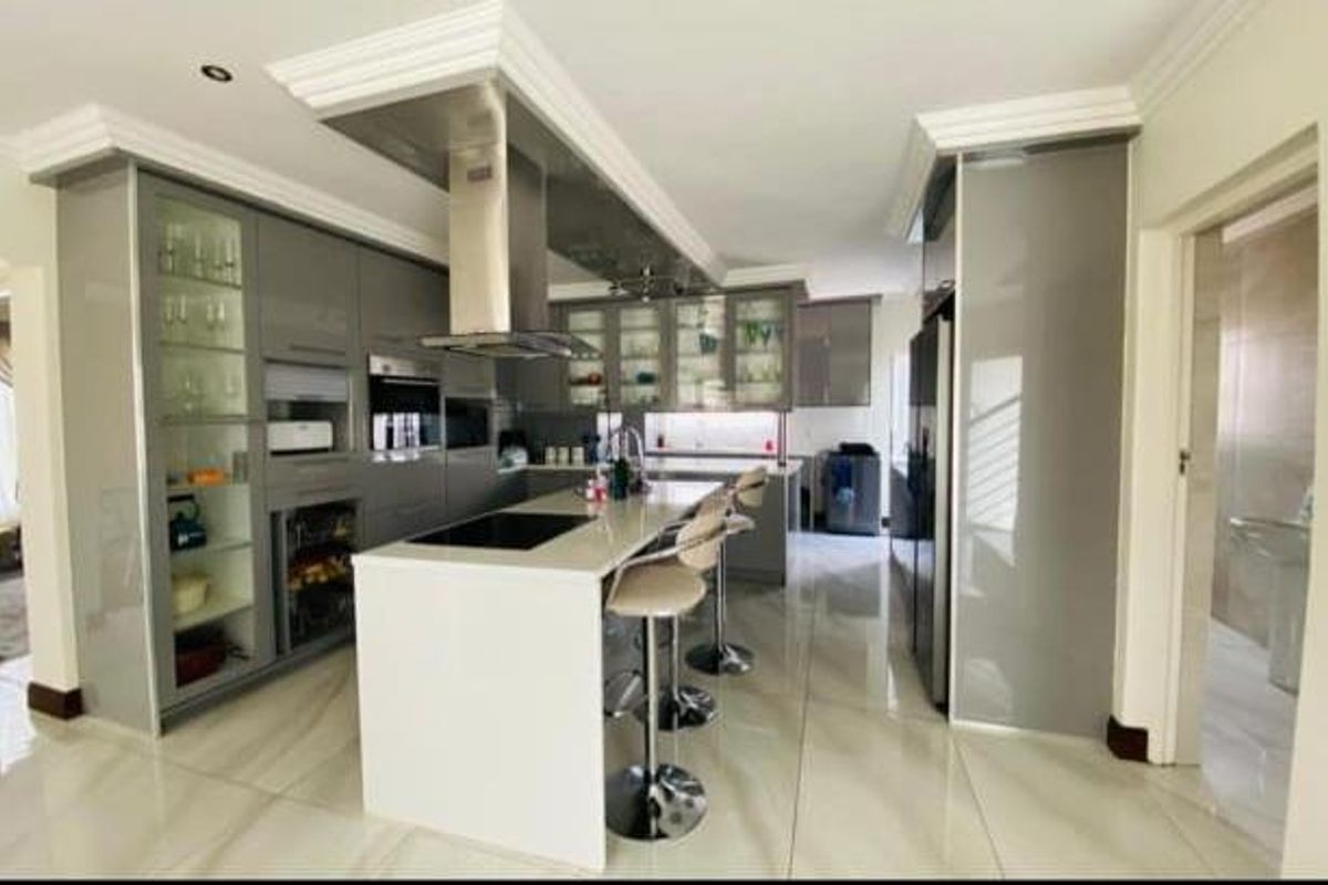Modern kitchen featuring high-gloss cabinetry, a central island with breakfast bar seating, integrated appliances, and sleek tiled flooring.