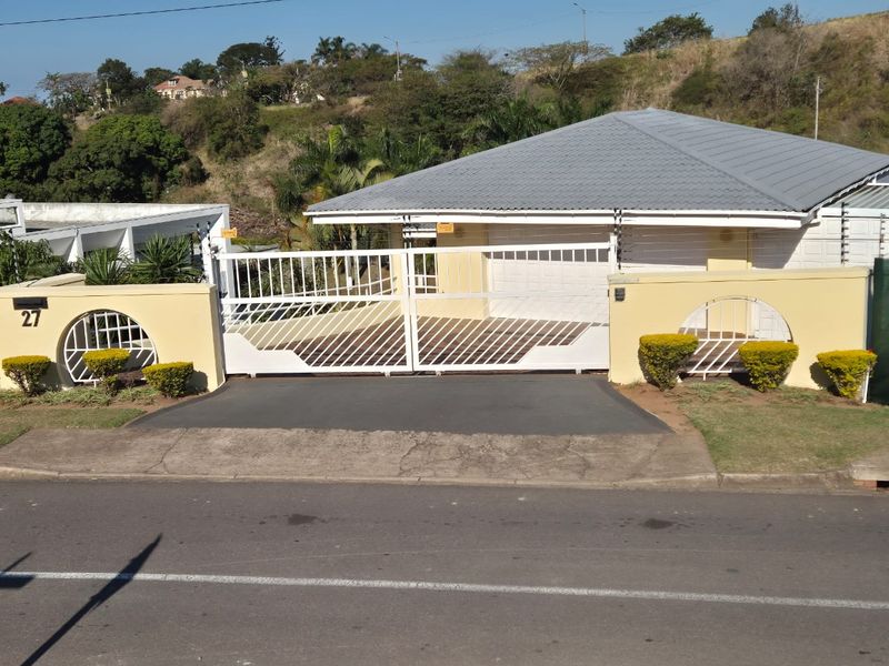 Front elevation of a residential property featuring a secure metal driveway gate, perimeter wall, and a tiled roof garage.