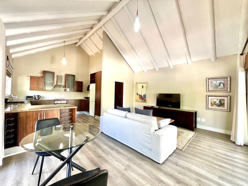 Spacious open-plan living area featuring a high vaulted ceiling with exposed beams, modern laminate flooring, and a well-appointed kitchen with integrated cabinetry.