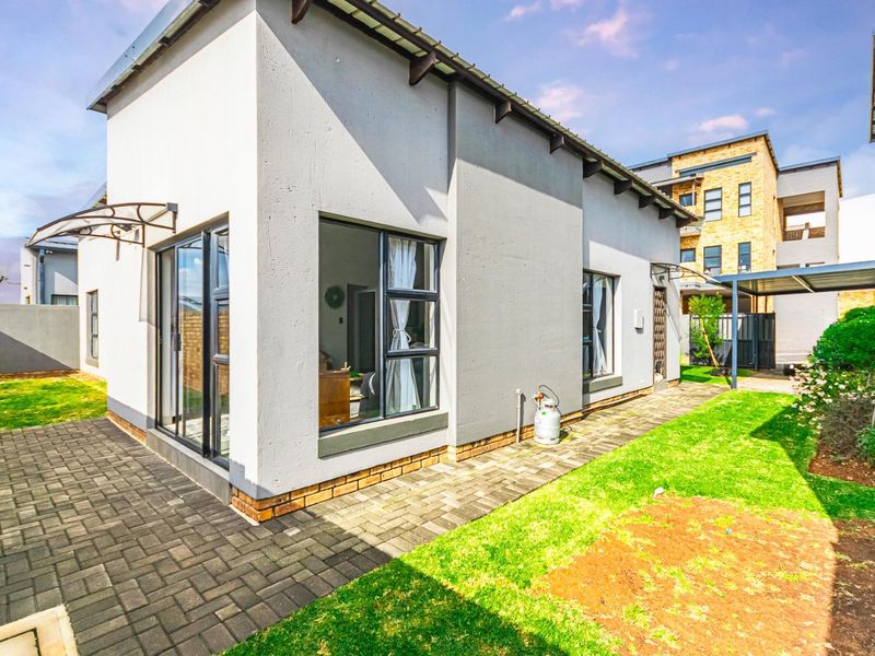 Rear view of the townhouse featuring a paved walkway, landscaped garden area, and modern aluminium window frames with sliding door access.