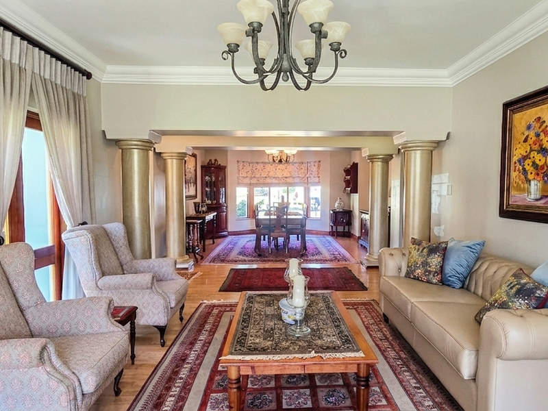 Spacious open-plan living and dining area featuring decorative columns, crown molding, and elegant chandelier lighting with access to outdoor space.