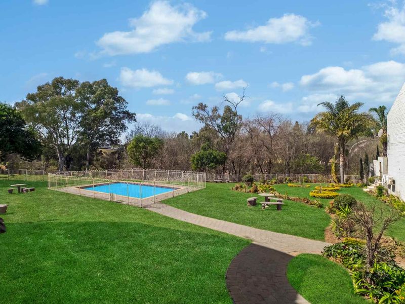 A well-maintained communal garden area featuring a fenced swimming pool and paved pathways, set within a landscaped outdoor space.