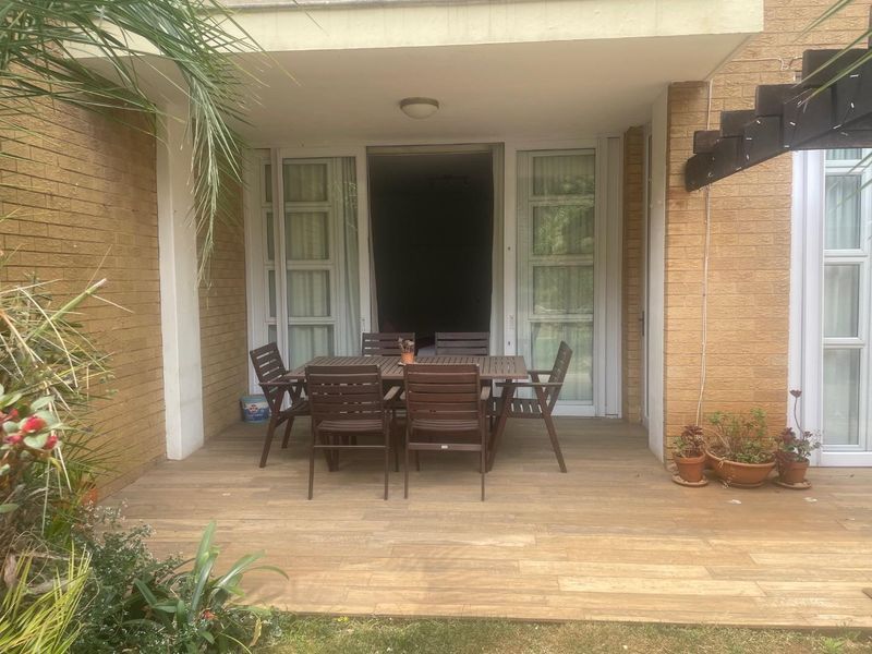 A covered patio area featuring wood-look tiled flooring, brick wall finishes, and sliding glass door access to the interior living space.
