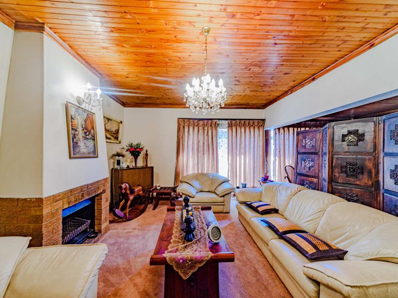 A cozy living room featuring a brick fireplace, warm timber tongue and groove ceiling, and elegant crystal chandelier lighting.
