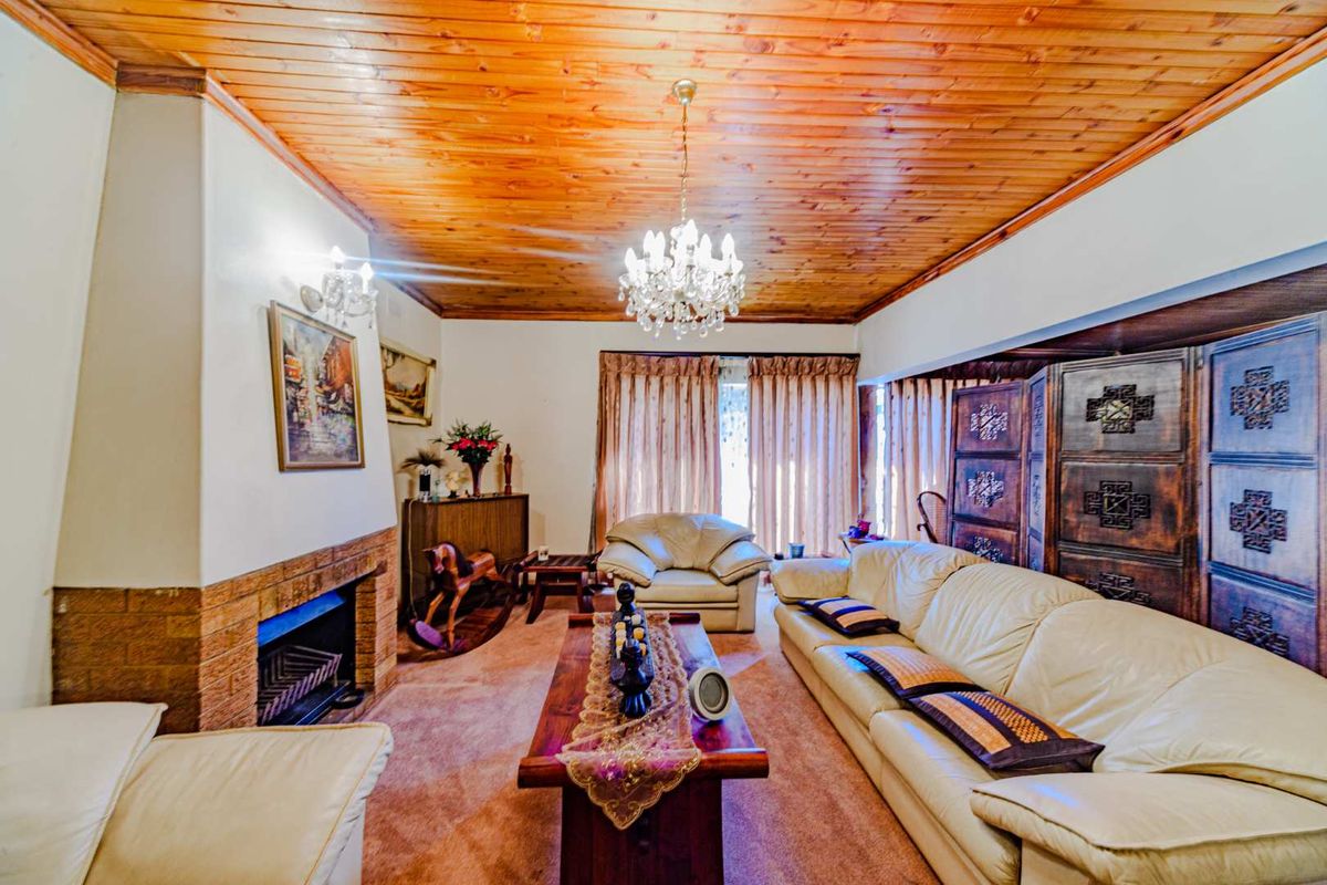 A cozy living room featuring a brick fireplace, warm timber tongue and groove ceiling, and elegant crystal chandelier lighting.