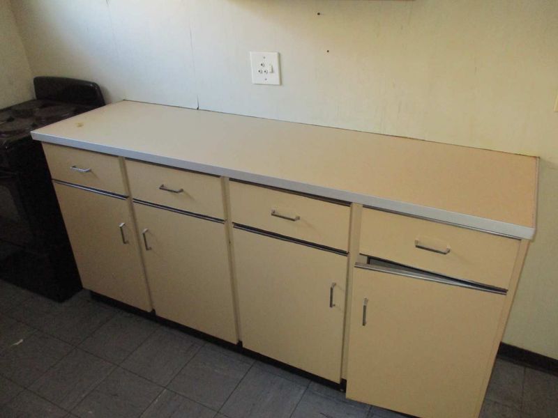 A dated kitchen area featuring original cabinetry, laminate countertops, and tiled flooring, requiring cosmetic updates to modernize the space.