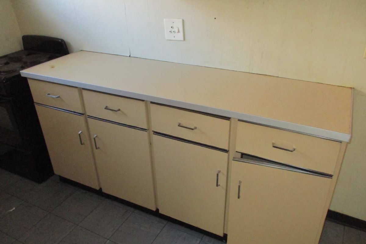 A dated kitchen area featuring original cabinetry, laminate countertops, and tiled flooring, requiring cosmetic updates to modernize the space.