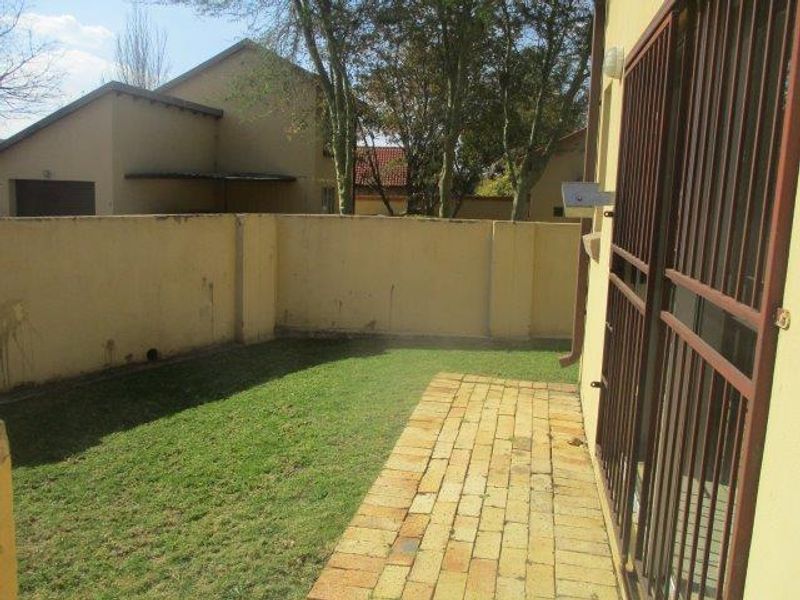 A private rear garden area featuring a small lawn, brick-paved patio, and secure access gate.
