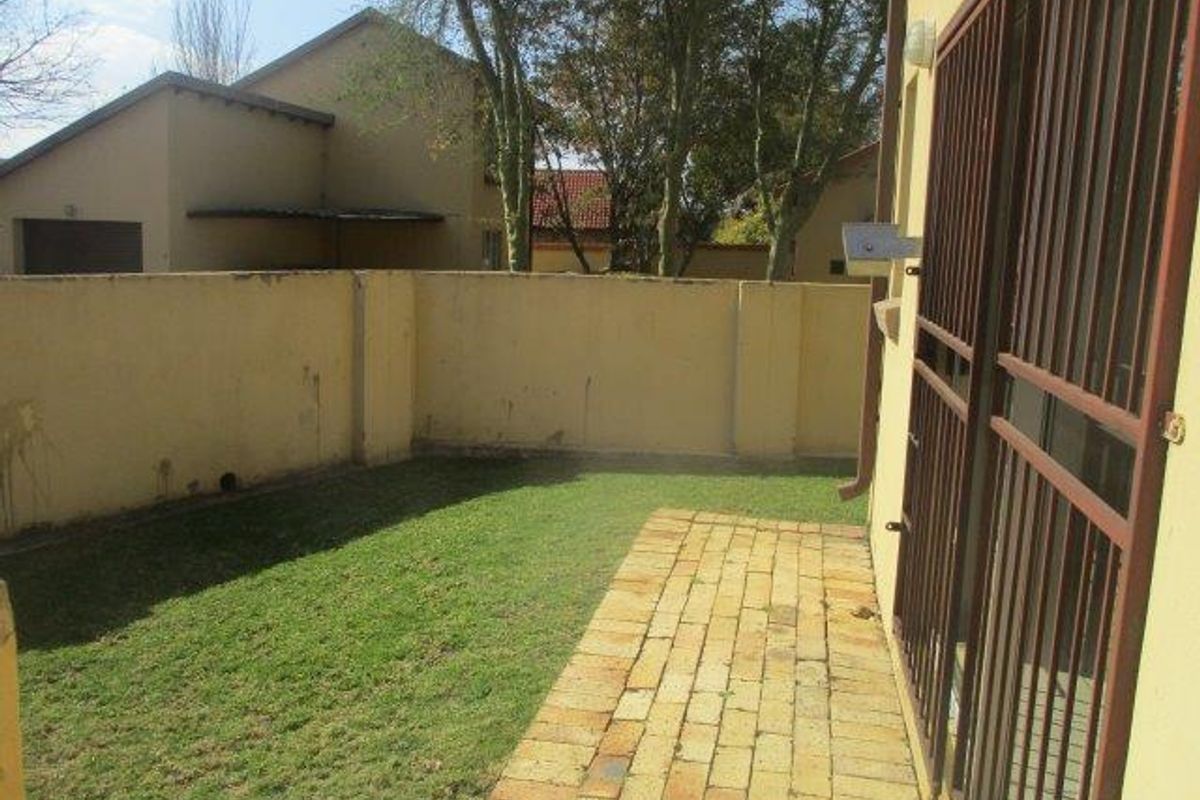 A private rear garden area featuring a small lawn, brick-paved patio, and secure access gate.