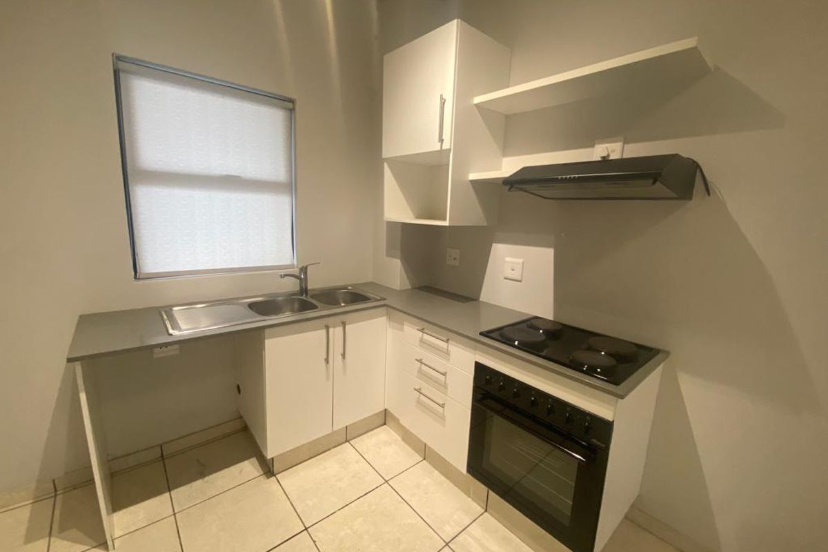 Compact kitchen featuring white cabinetry, grey countertops, a built-in oven with hob, extractor fan, and a double-basin sink.