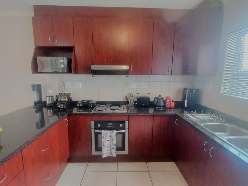A functional kitchen featuring dark wood cabinetry, granite countertops, a built-in oven with hob, and a double sink with natural light from the window.