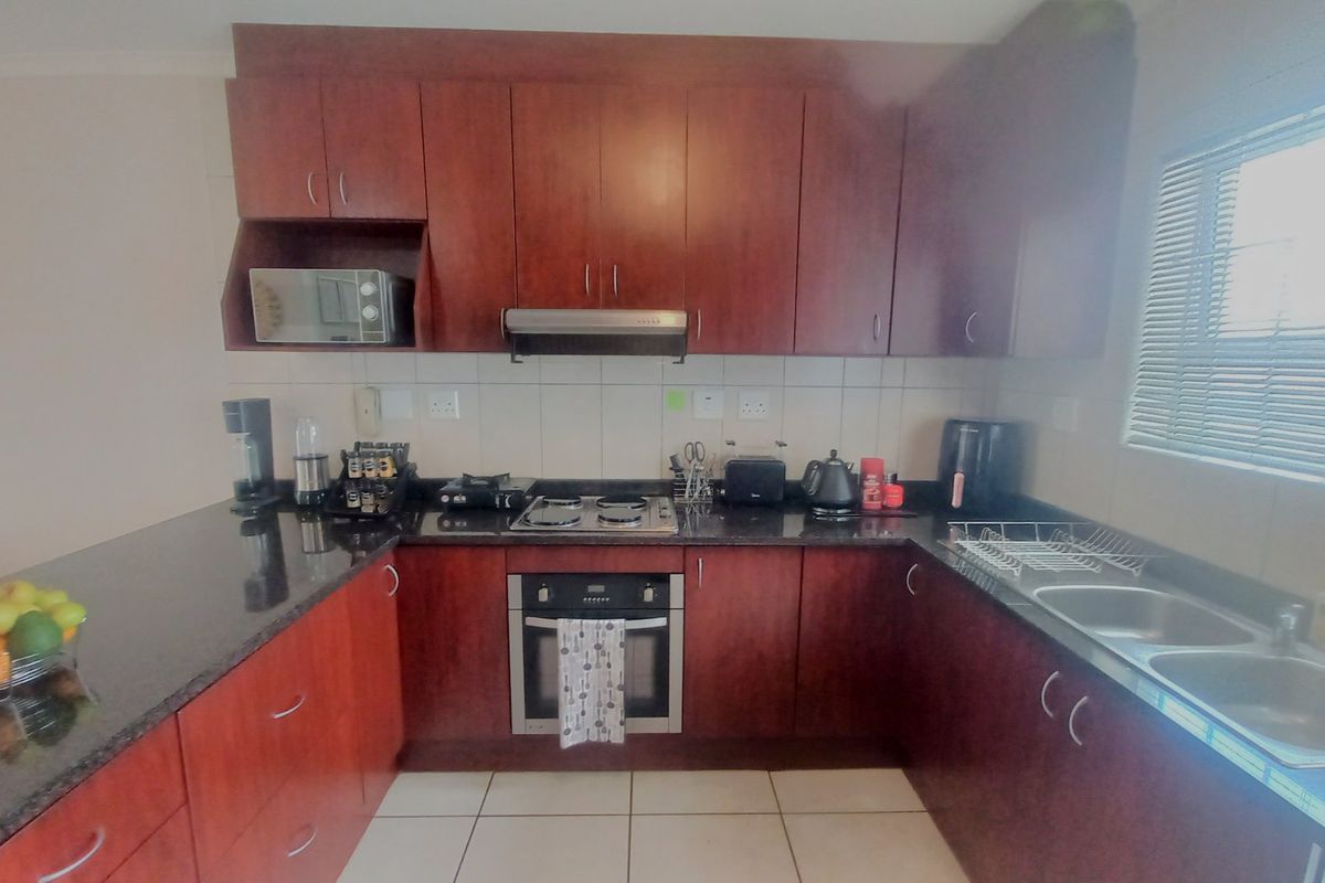 A functional kitchen featuring dark wood cabinetry, granite countertops, a built-in oven with hob, and a double sink with natural light from the window.