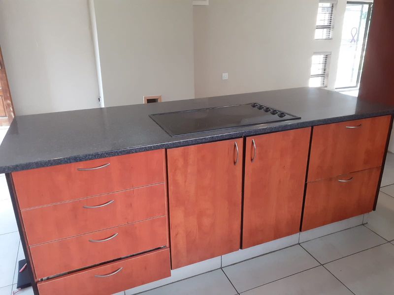 A functional kitchen island featuring a built-in hob, stone countertop, and ample storage cabinetry, set against a neutral interior space with tiled flooring.