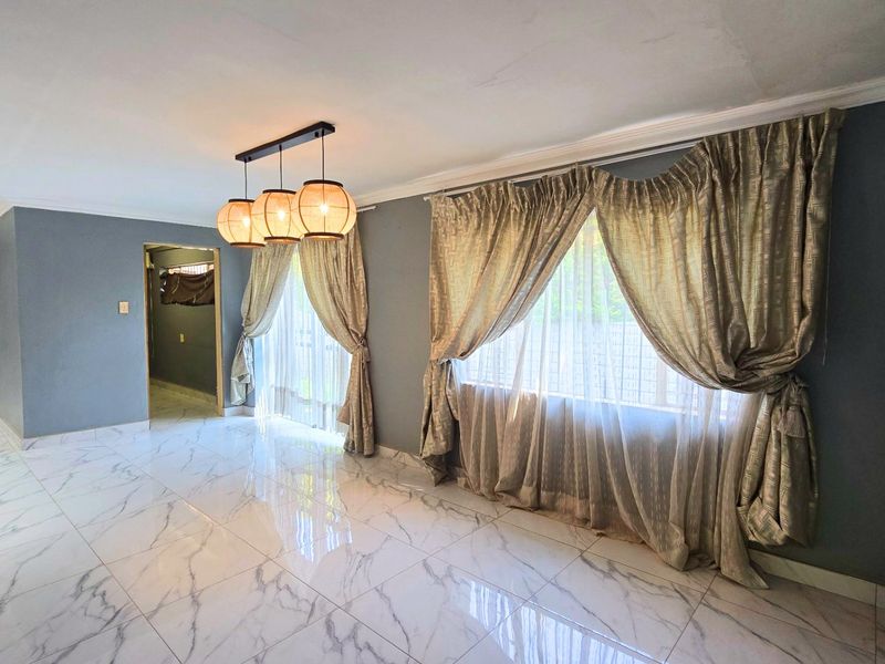 Spacious living area featuring polished marble-look floor tiles, modern pendant lighting, and large windows with elegant drapery.