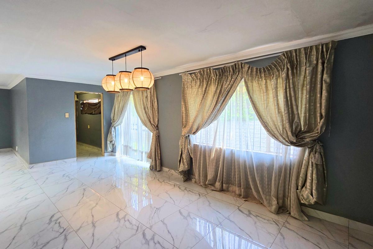 Spacious living area featuring polished marble-look floor tiles, modern pendant lighting, and large windows with elegant drapery.