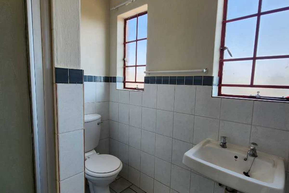 A functional bathroom featuring a shower enclosure, wall-mounted basin, and toilet, finished with tiled flooring and wall splashbacks.