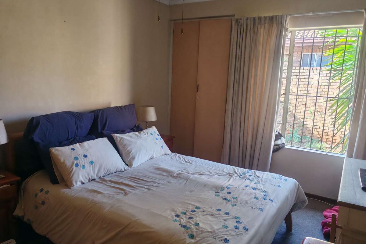 A bedroom featuring built-in cupboards and security bars on the window, requiring cosmetic updates to improve the overall finish.