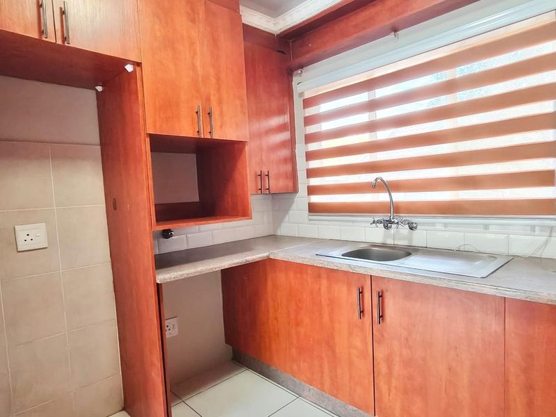 A functional kitchen featuring wooden cabinetry, laminate countertops, a stainless steel sink, and tiled flooring with a neutral backsplash.