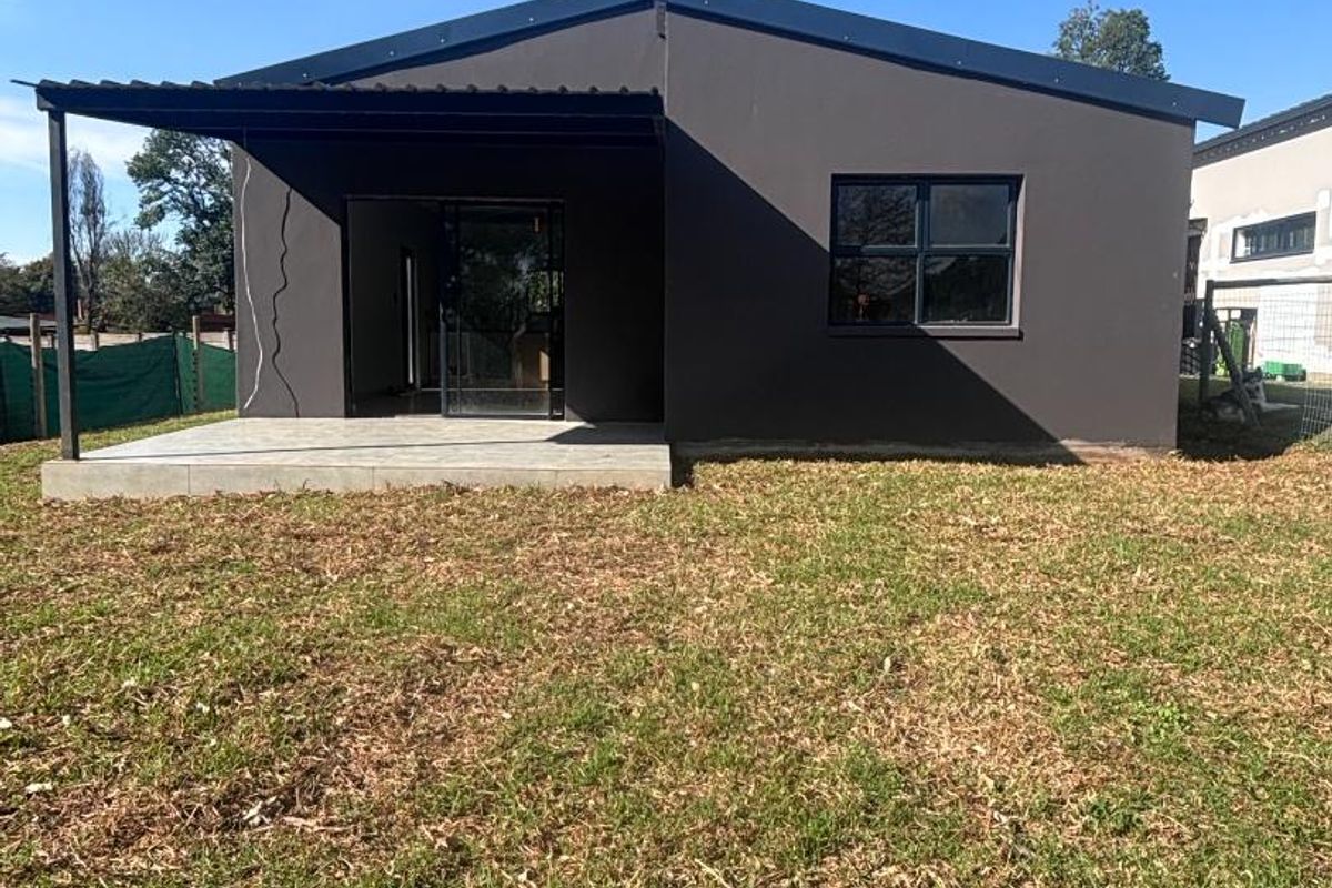 Rear view of the townhouse featuring a covered patio area, dark exterior finish, and a private garden space.