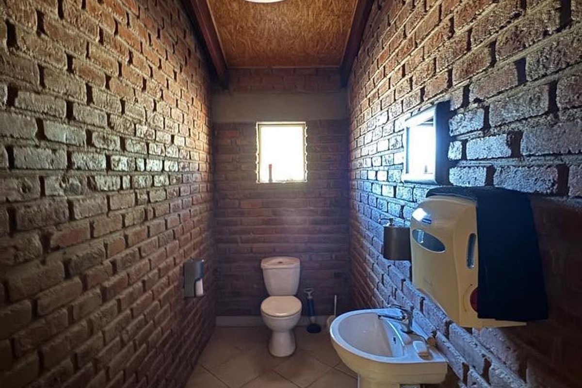 A rustic bathroom featuring exposed brick walls, a pedestal basin, and a unique timber ceiling panel, providing a distinct industrial aesthetic.