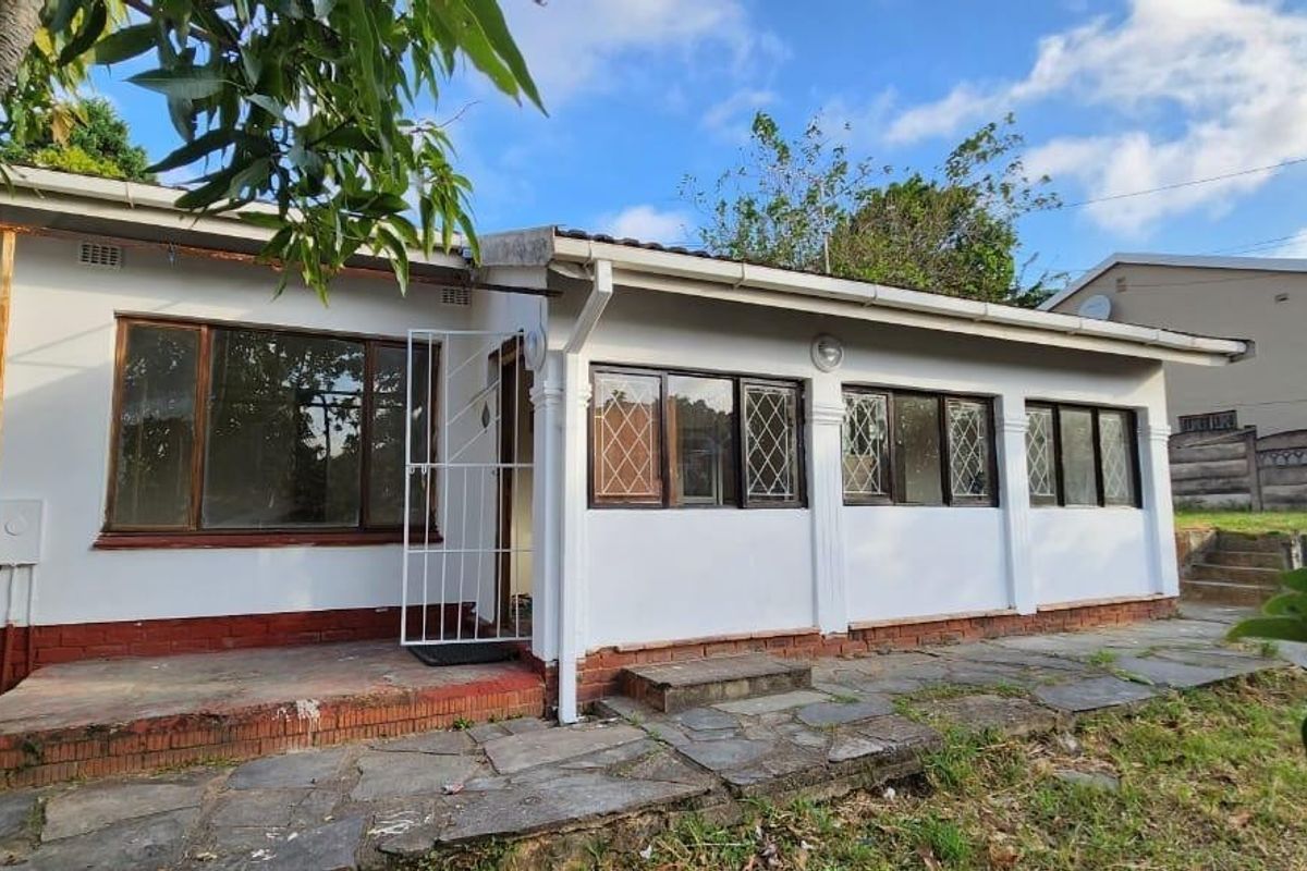 Rear exterior view of the house featuring a stone paved patio, white rendered walls with brick plinth, and metal framed windows.