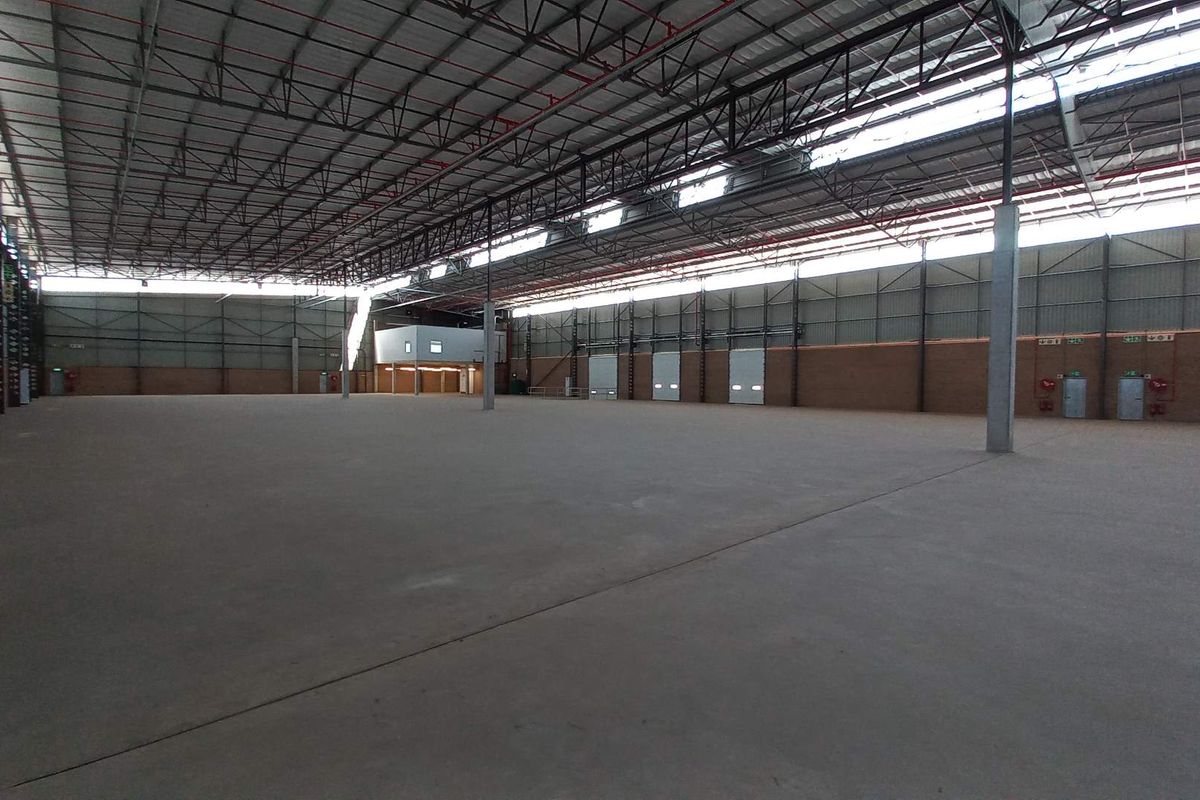 Expansive industrial warehouse space featuring high ceilings with exposed steel trusses, concrete flooring, and multiple roller shutter doors for efficient logistics access.