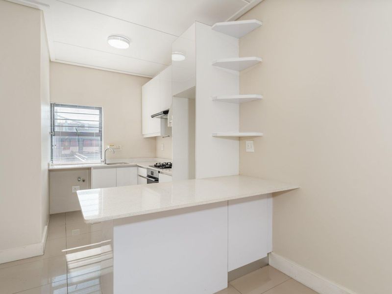 Modern, clean-lined kitchen featuring white cabinetry, stone countertops, a breakfast bar, and integrated appliances, finished with neutral tiled flooring.