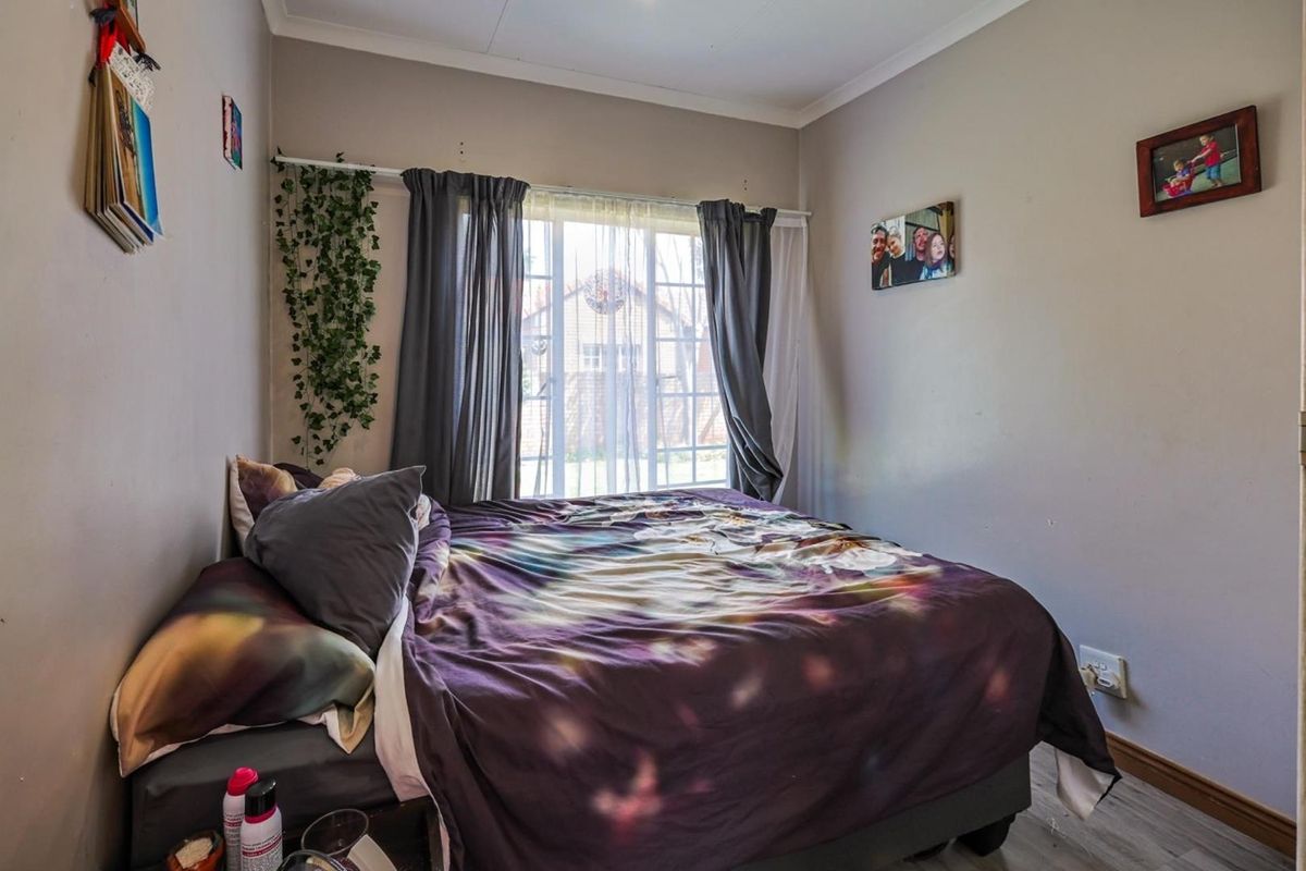 A standard bedroom featuring laminate flooring, a window with curtain tracks, and neutral wall finishes.